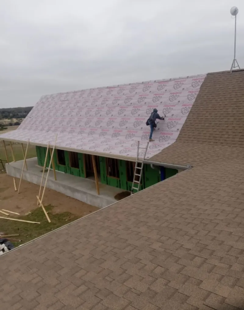 Worker preparing underlayment for a metal roof installation in Raymore